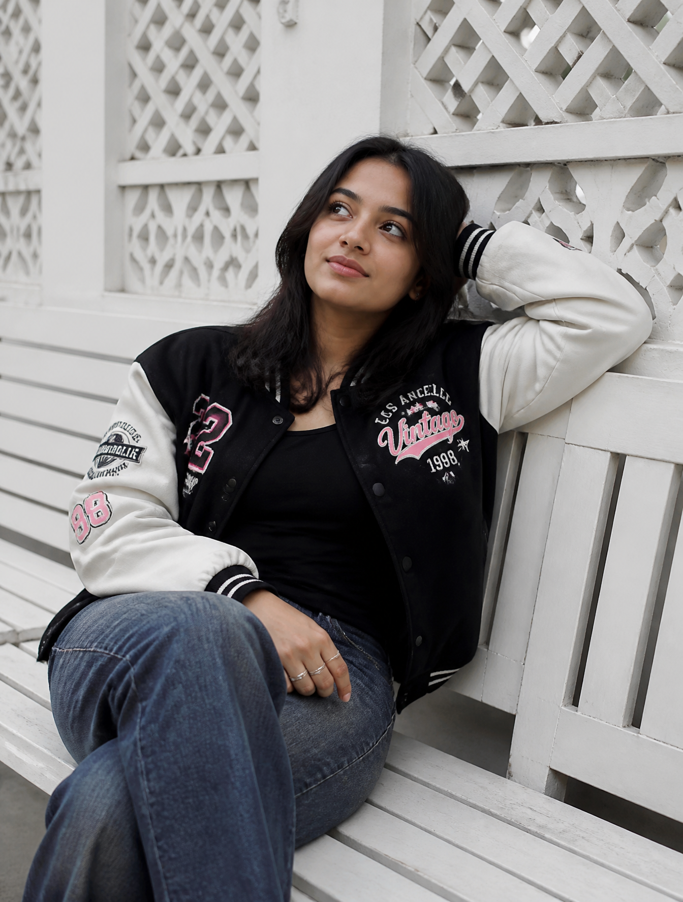A young woman is sitting casually on a white wooden bench...